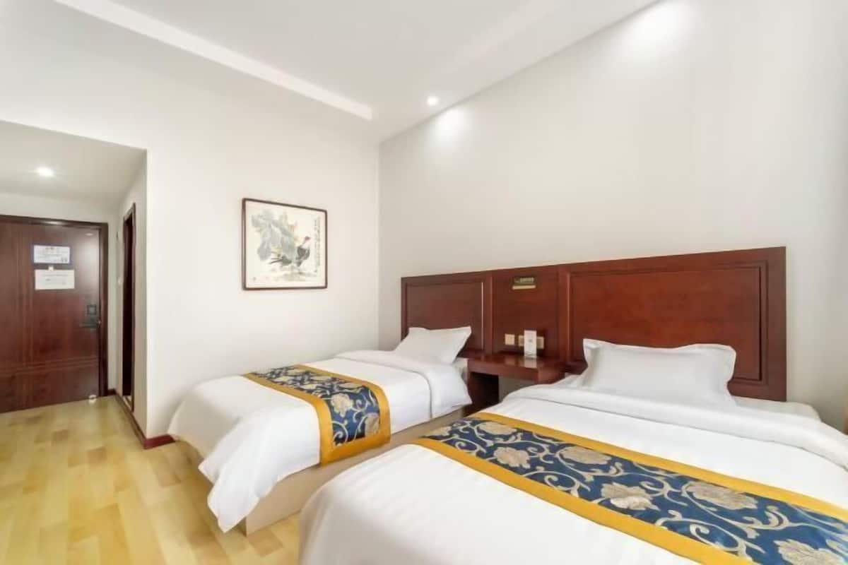 A hotel room with two beds, wooden headboards, a framed picture on the wall, and a wooden floor.