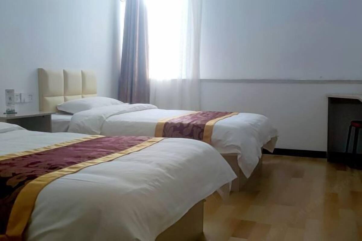 A hotel room with two beds, a nightstand, a window with curtains, and a wooden floor.