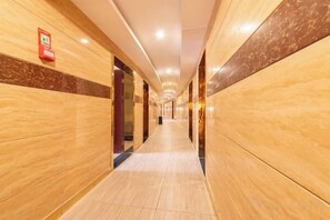 Un couloir d’hôtel aux murs de marbre, avec un détecteur d’incendie et un long couloir.