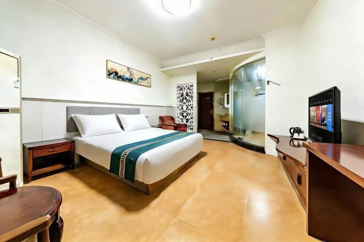 Ein Hotelzimmer mit Bett, Nachttisch, Sessel, Fernseher und Spiegel.