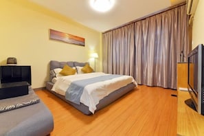 A hotel room with a bed, a TV, a desk, and a large window with curtains.