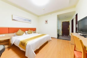 A hotel room with a bed, a desk with a TV, a chair, and a door leading to another room.