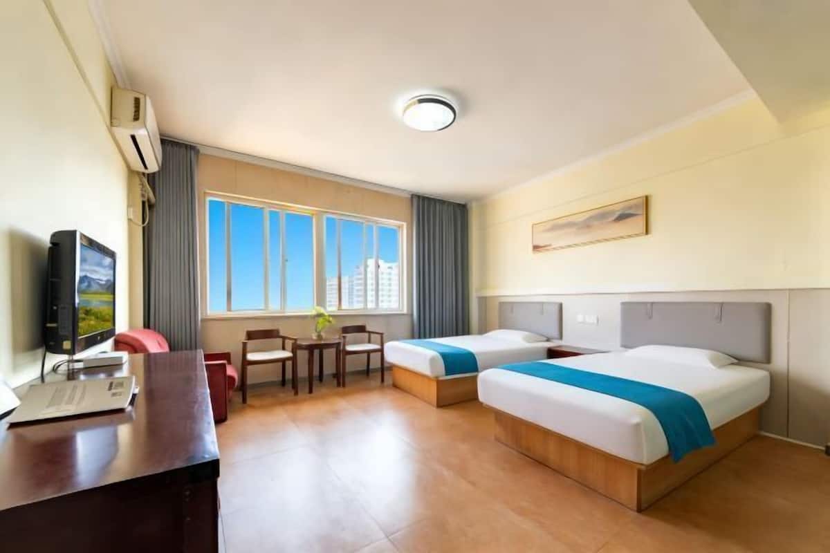 Ein Hotelzimmer mit zwei Betten, einem Schreibtisch, einem Fernseher und einem Fenster mit Blick auf die Stadt.