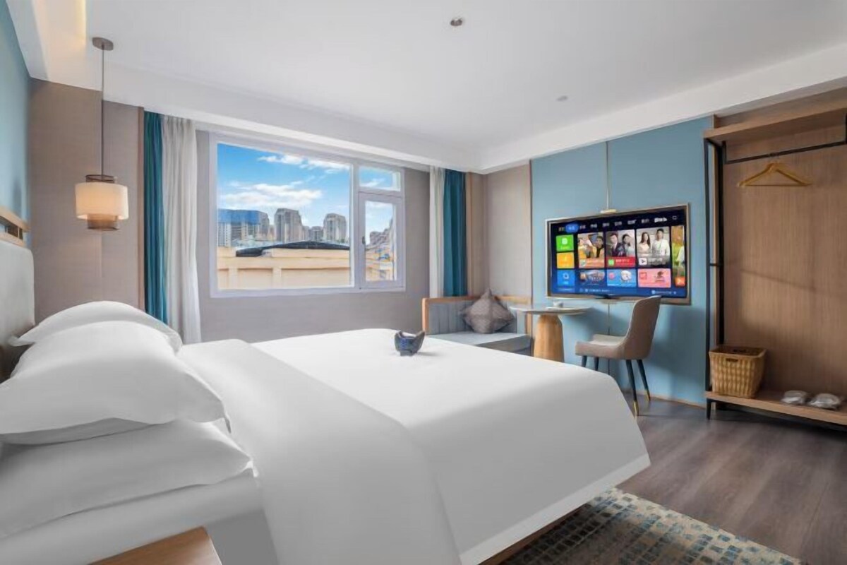 Une chambre d’hôtel équipée d’un lit, d’un bureau, d’une chaise, d’une télévision et d’une fenêtre donnant sur la ville.