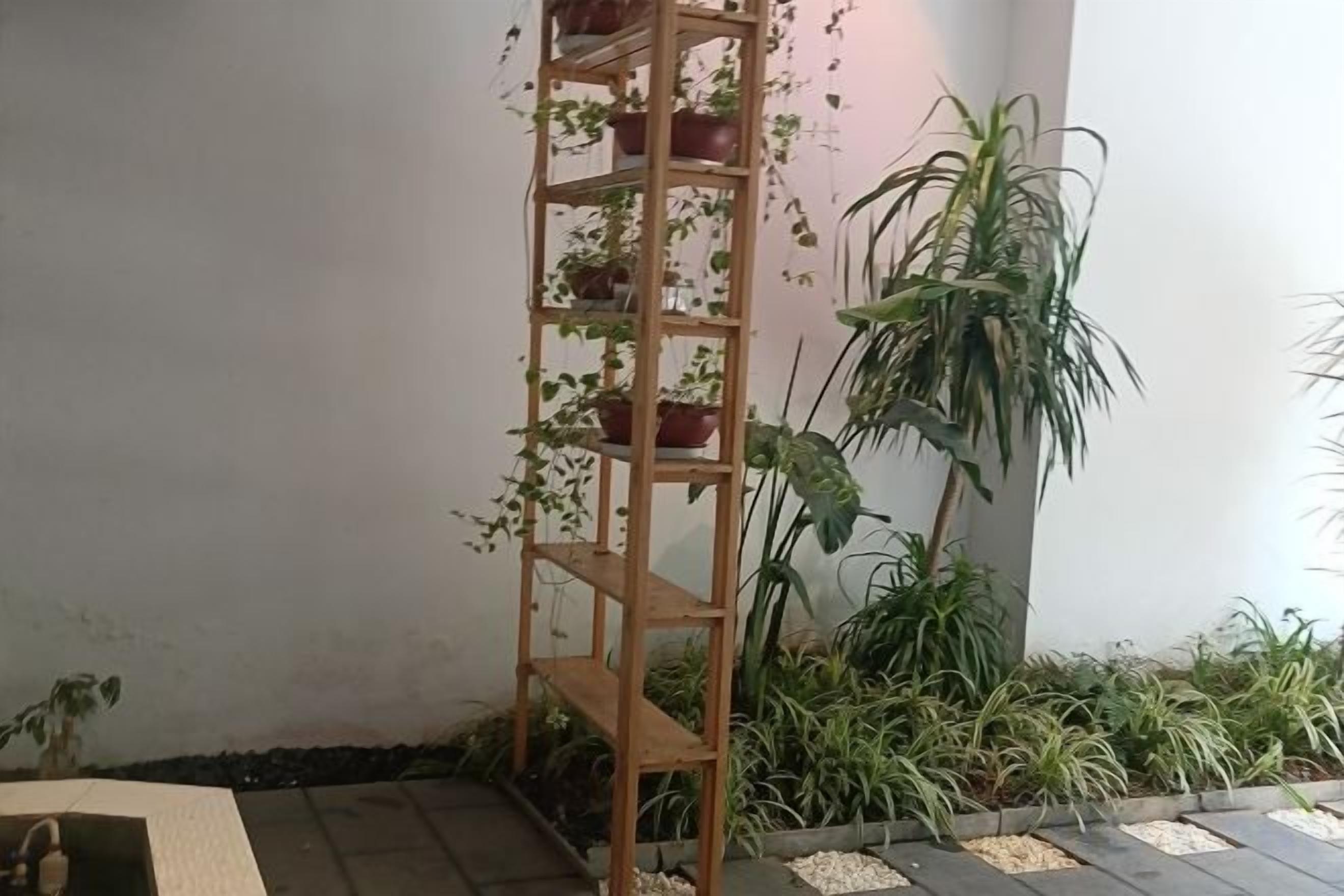 A corner with a wooden plant shelf holding potted plants, a tall potted plant, and a small garden area with pebbles.