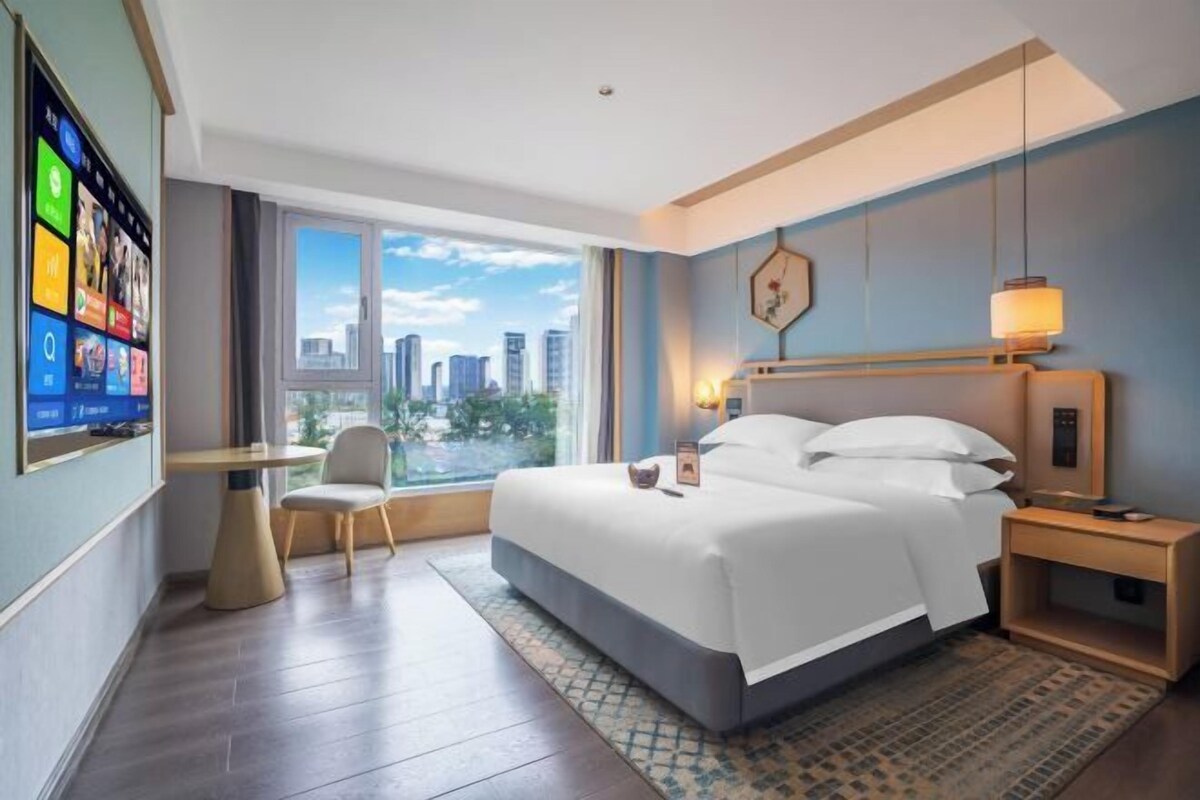 Une chambre d’hôtel avec un grand lit, un bureau, une chaise, une télévision et une vue sur la ville.