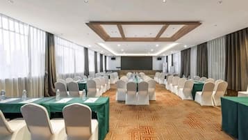 A conference room with rows of tables and chairs, a projector screen, and a patterned carpet.