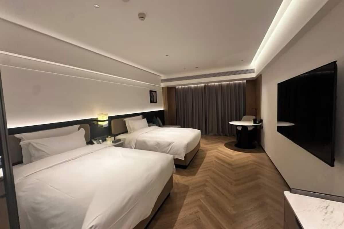 A hotel room with two beds, a TV, a desk, and a chair.