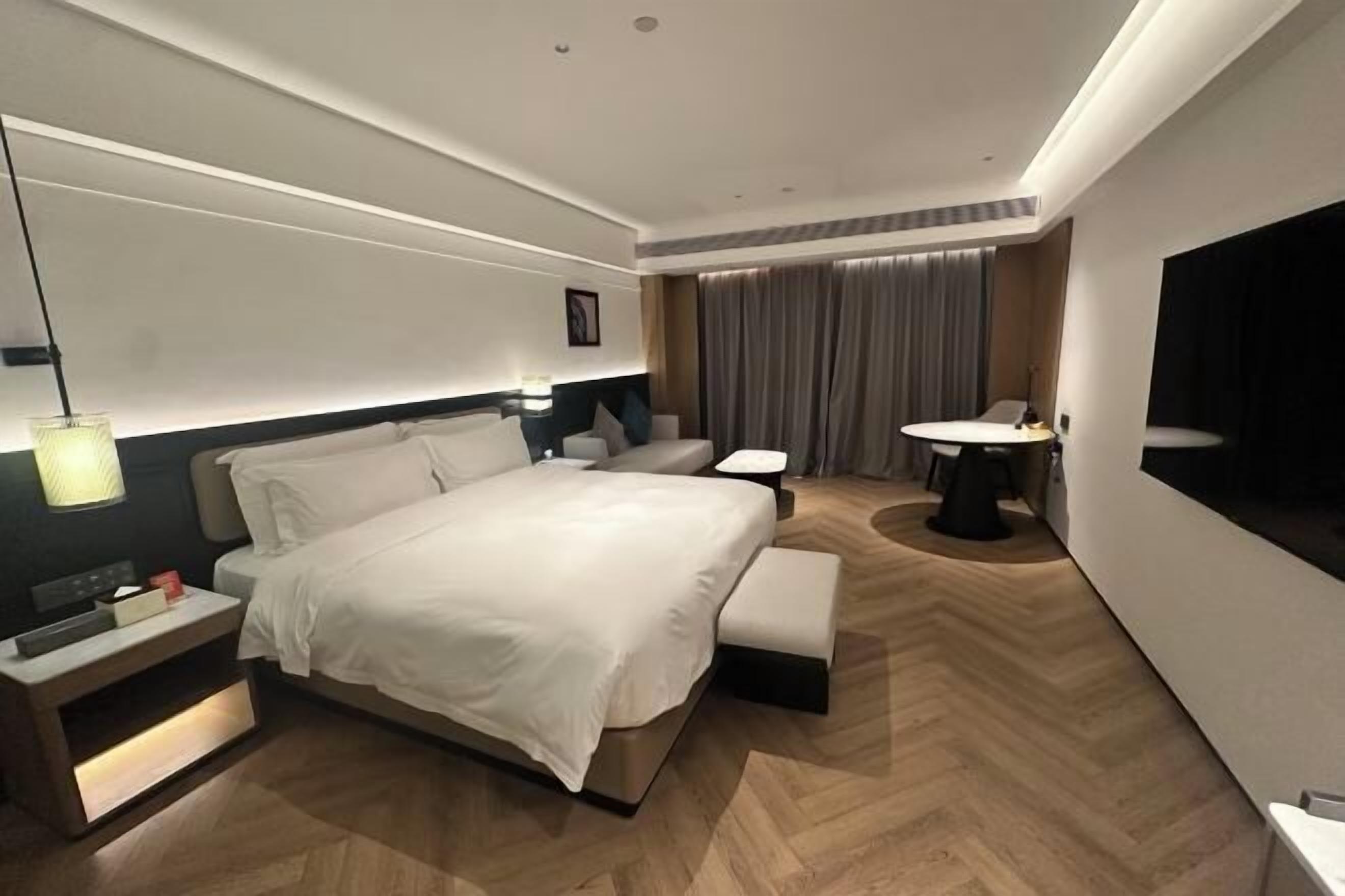 Une chambre d’hôtel moderne avec un grand lit, des tables de chevet, un bureau, une chaise, une table ronde et un téléviseur.