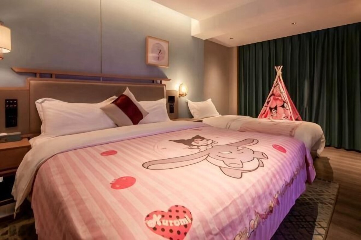 A hotel room with a large bed, a headboard, a bedside table, a wall clock, and a window with curtains.