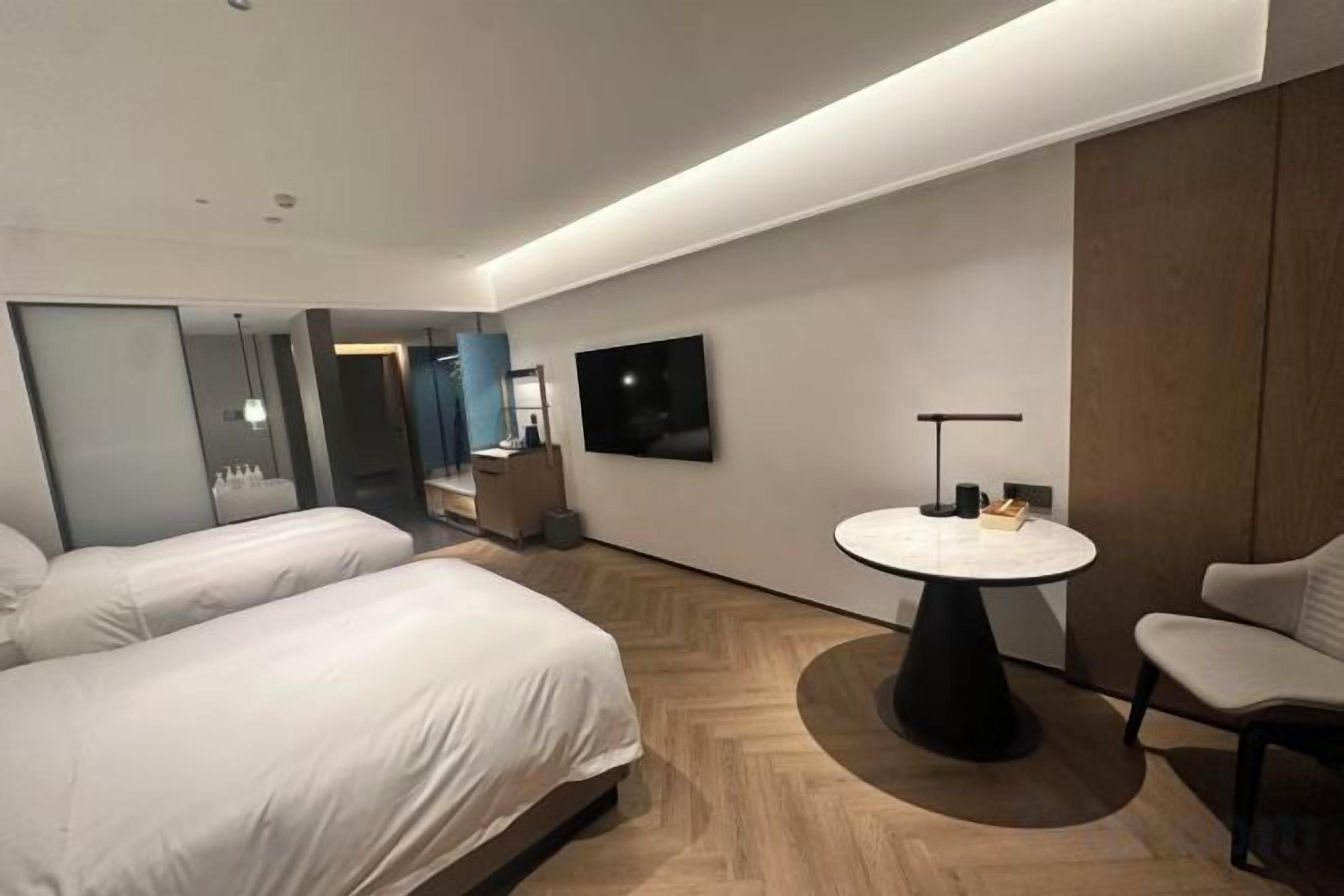 A modern hotel room with two beds, a round table, and a TV on the wall.