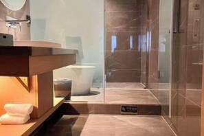 Un baño moderno con piso de mármol, cabina de ducha de vidrio y tocador de madera.