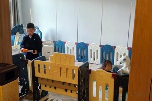 Ein Zimmer mit einem Bett, einem spielenden Kind und einem Kind, das an einem Tisch sitzt.