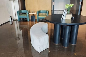 Un hall d’entrée avec une table ronde, deux fauteuils turquoise, un canapé blanc et une petite table d’appoint.
