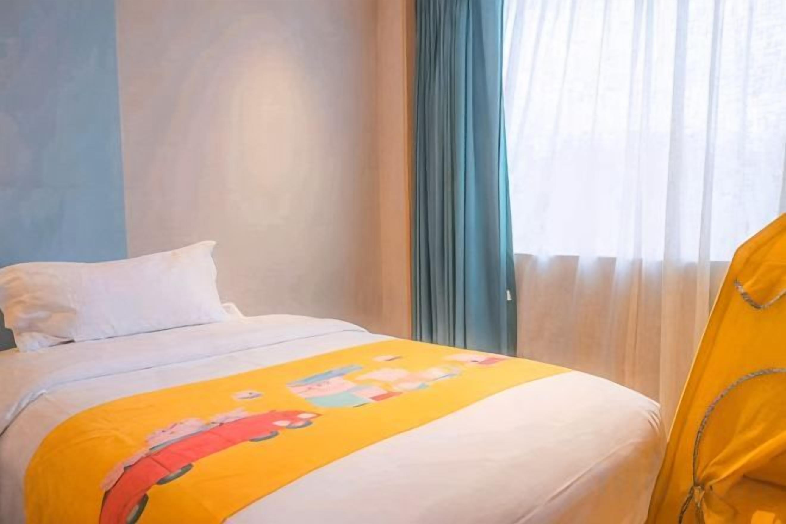 A hotel room with a bed, a window with curtains, and a yellow blanket.
