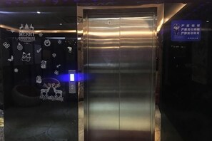 An elevator with a metallic finish, a sign indicating 'Merry Christmas,' and a digital display with text. - Ai Jiu Hotel (Shanghai)