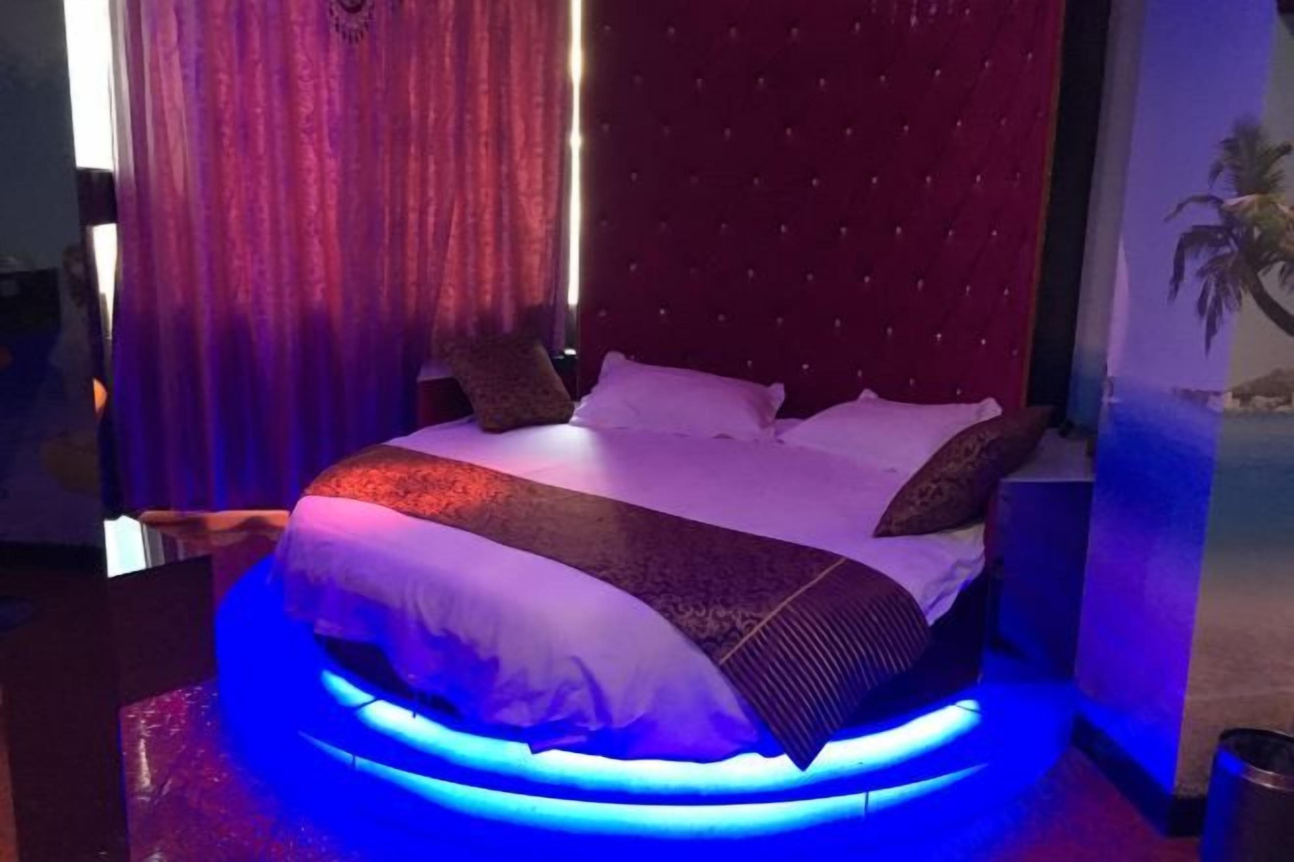 A bed with a red headboard, white bedding, and a blue illuminated base.