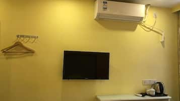 A room with a mounted TV, a white shelf with a kettle, and a wall-mounted air conditioner.
