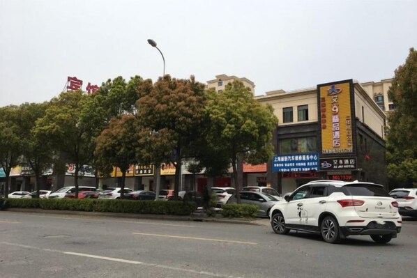 A street with parked cars, trees, and buildings with signage. - Ai Jiu Hotel (Shanghai)