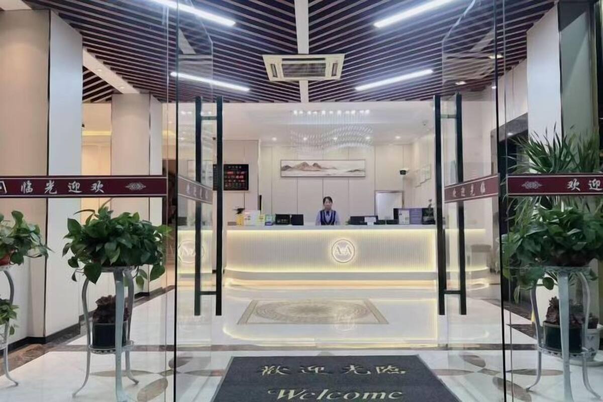 Un espace d’accueil d’hôtel au design moderne, comprenant un comptoir de réception, un réceptionniste et des plantes en pot.