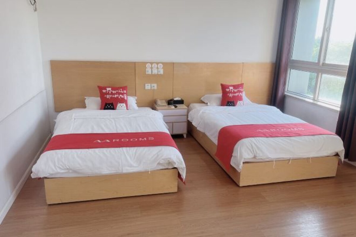 A hotel room with two beds, each with a wooden headboard, white bedding, and red accents. There is a nightstand between the beds with a phone and a small table.