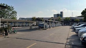 Un estacionamiento con automóviles, una zona techada y un edificio al fondo.