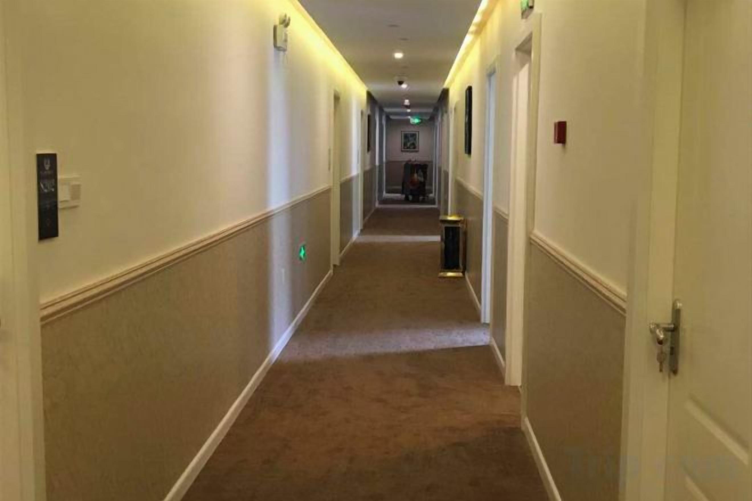 A hotel corridor with doors on both sides, a trash bin, and a light switch on the wall.