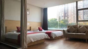 Een hotelkamer met twee bedden, een slaapbank, grote ramen en uitzicht op hoogbouw.