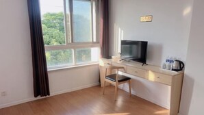 Una habitación con un escritorio de madera, una silla, un televisor y un ventanal con cortinas.