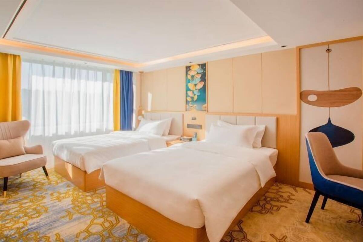 A hotel room with two beds, a desk, a chair, and a painting on the wall.