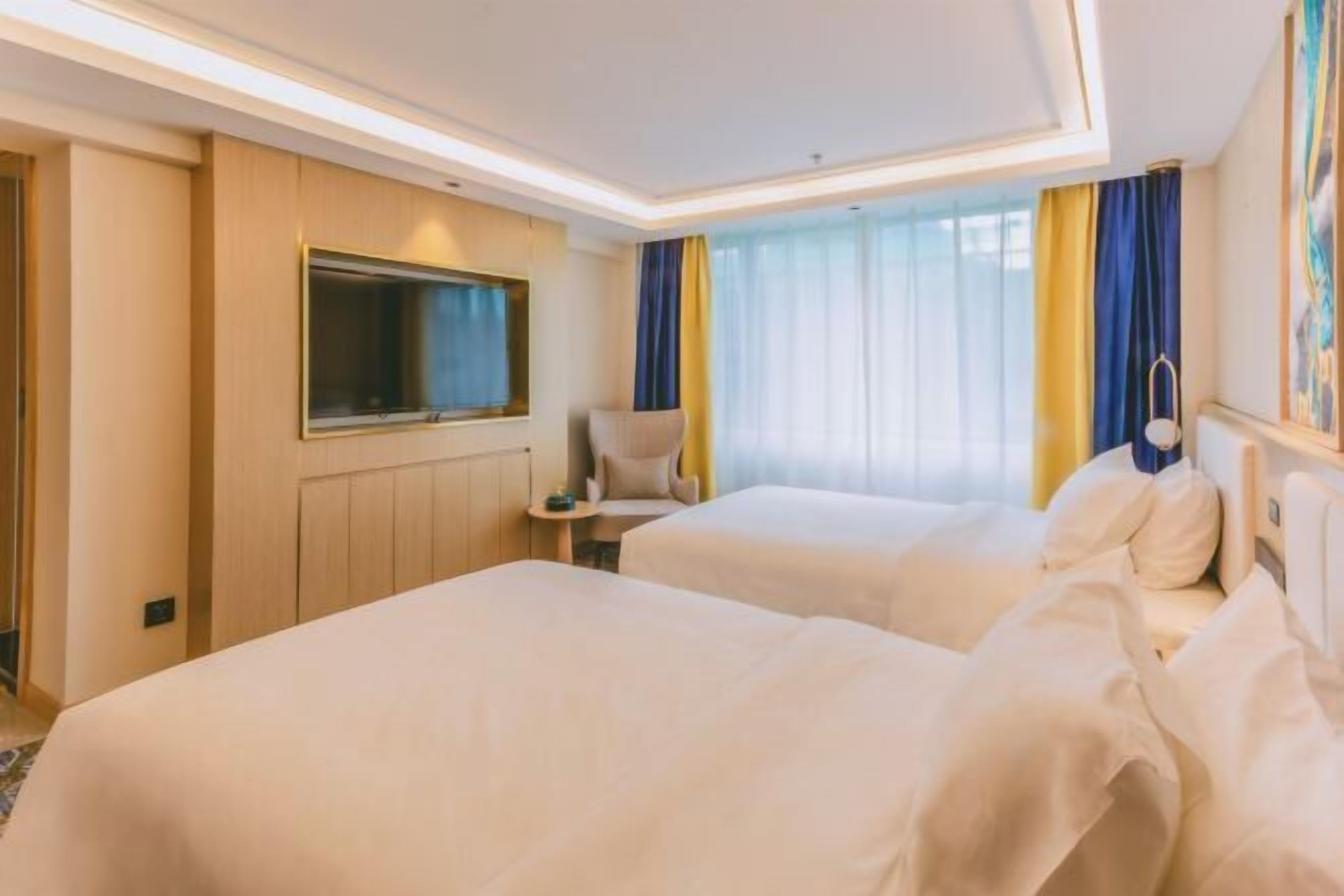 Habitación de hotel con dos camas, televisión, una silla y ventana con cortinas.