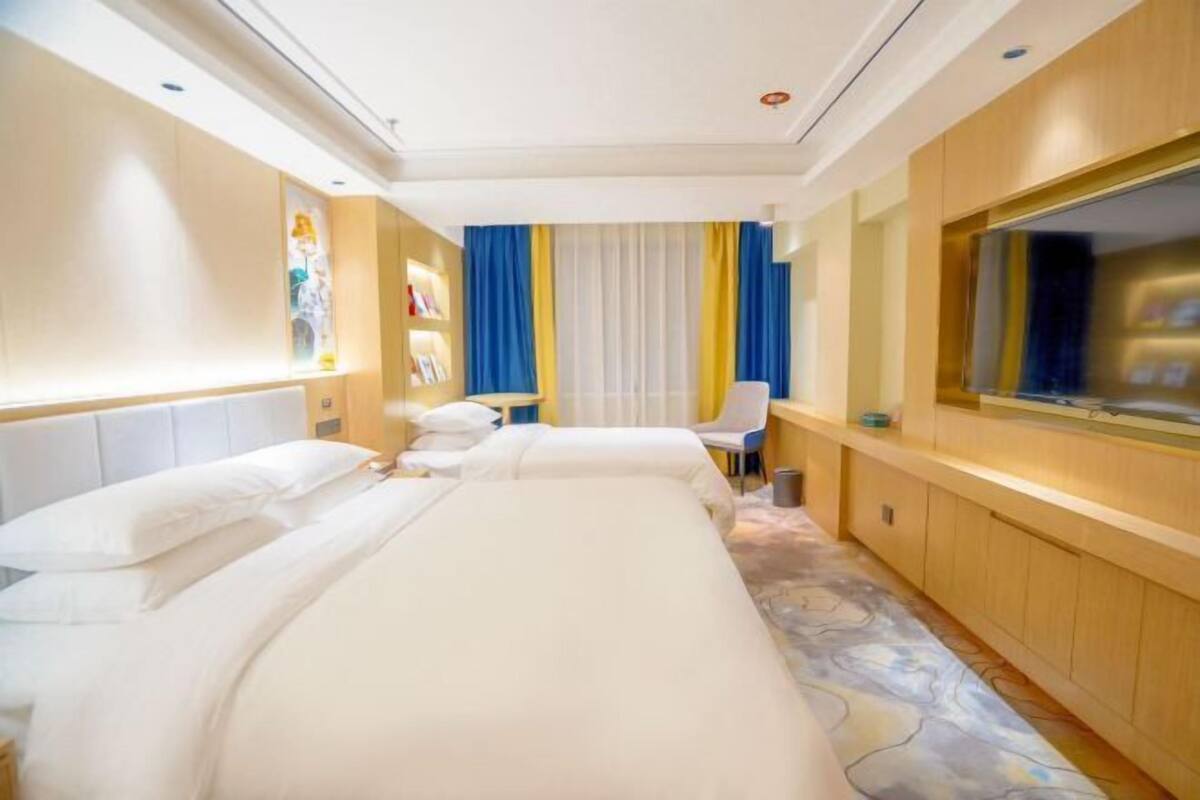 A hotel room with two beds, a desk, a chair, a TV, and a window with curtains.