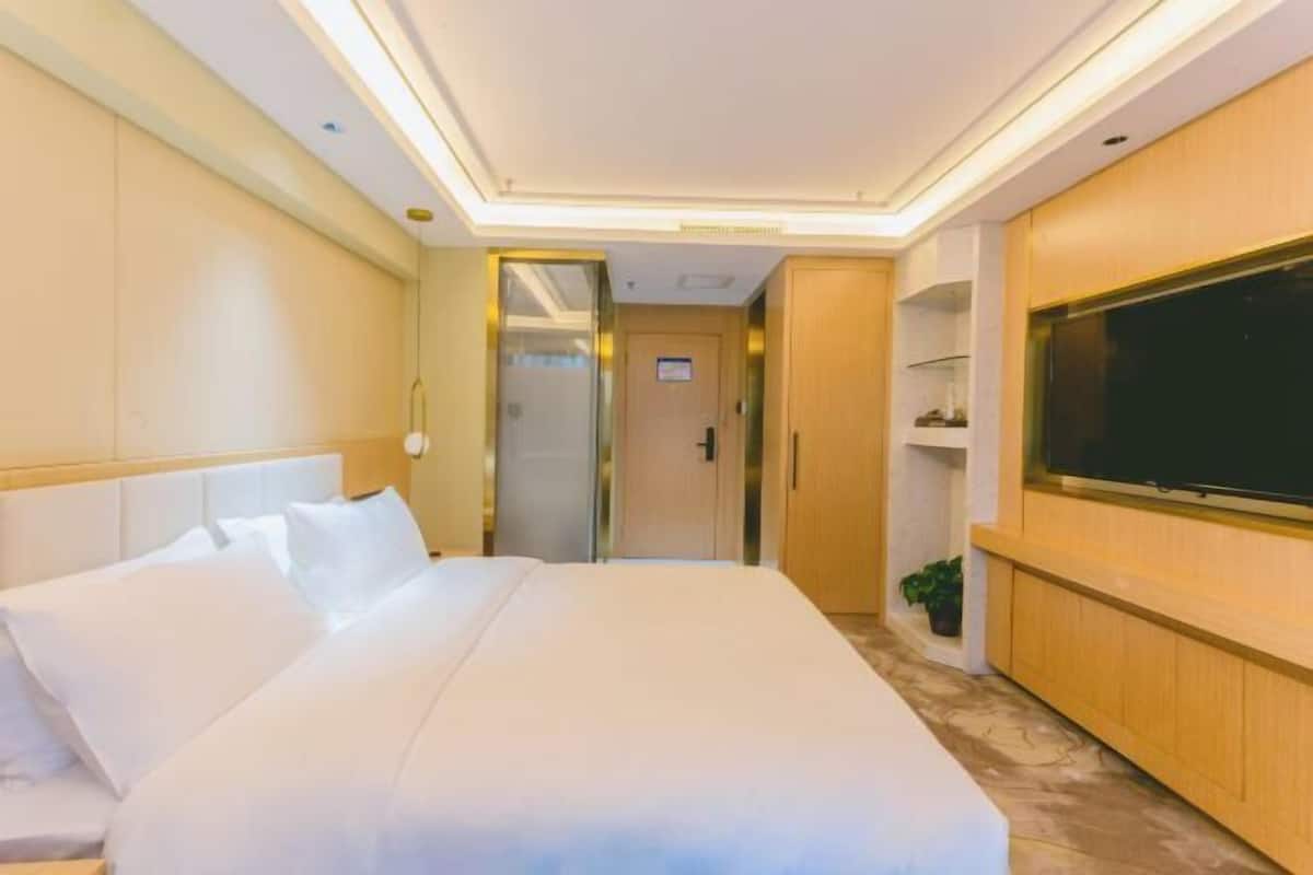 A hotel room with a large bed, a television on the wall, and a door leading to another room.