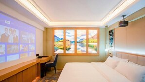 Una habitación de hotel con una cama, un escritorio con una silla, una pantalla de proyector y un ventanal con vistas panorámicas.