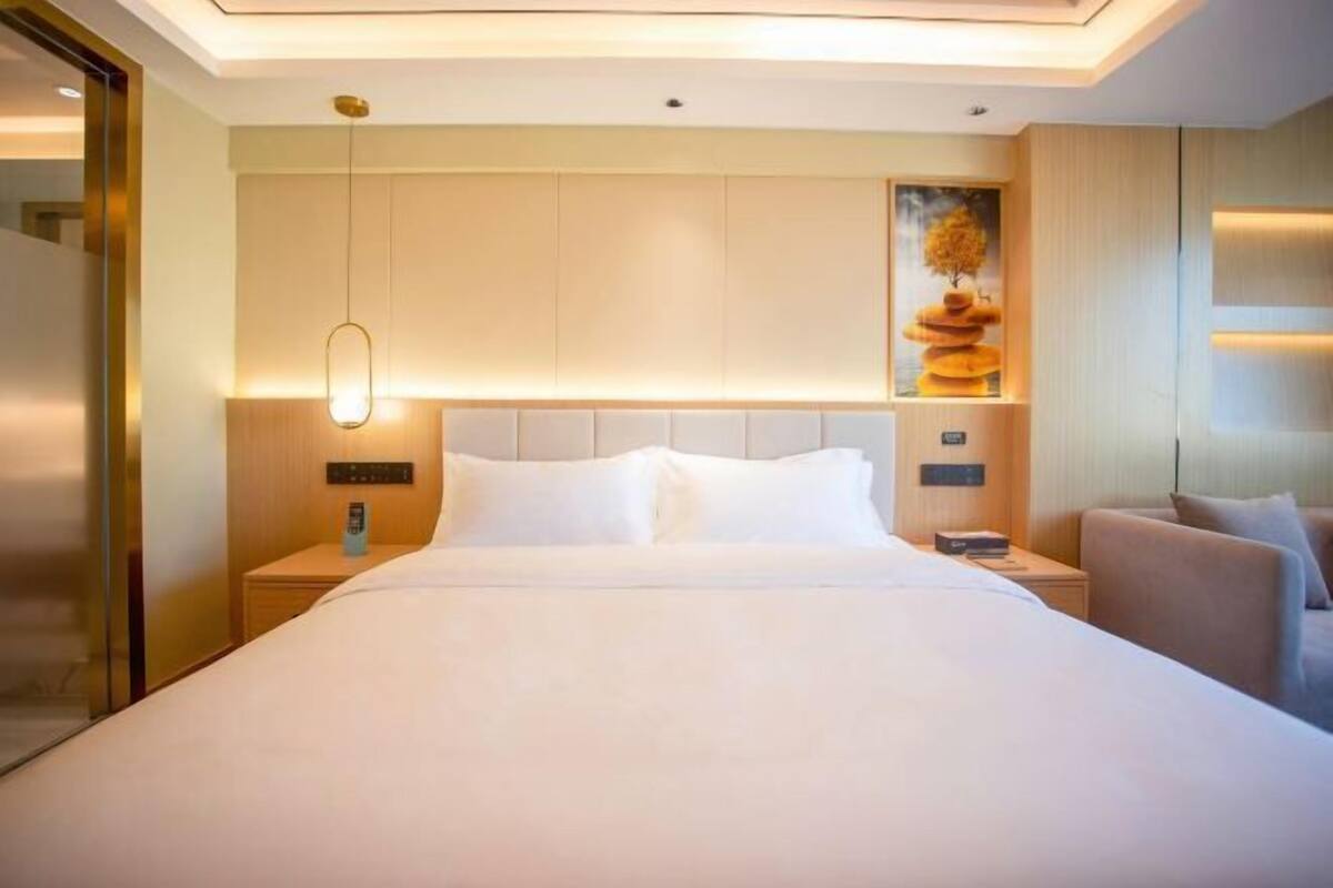 A modern hotel room with a large bed, bedside tables, a wall-mounted light, and a painting.