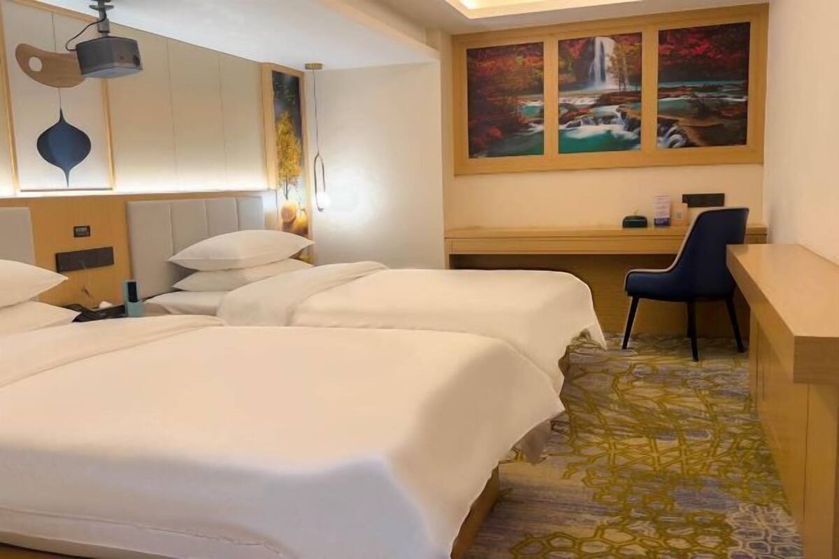 A hotel room with two beds, a desk, and a chair. There is a painting of a waterfall on the wall.