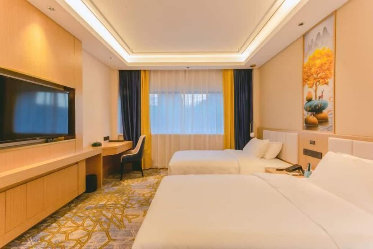 A hotel room with a TV, two beds, a desk, and a chair.