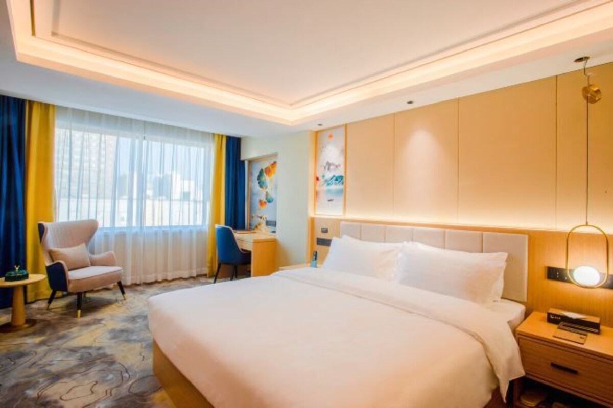 A hotel room with a large bed, a desk, a chair, and a nightstand with a lamp.