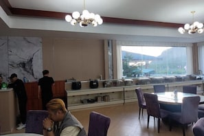 A hotel dining area with a marble wall, a long counter with a barista, and a view through large windows.