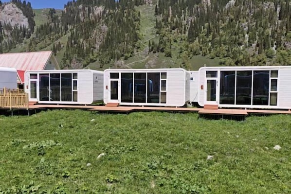 Una hilera de viviendas modulares blancas con ventanales amplios, frente a un paisaje montañoso.
