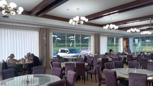 A spacious dining area with round tables and purple chairs, large windows with a view of the outside, and a modern chandelier. - Aketasi Resort (Nilka County)
