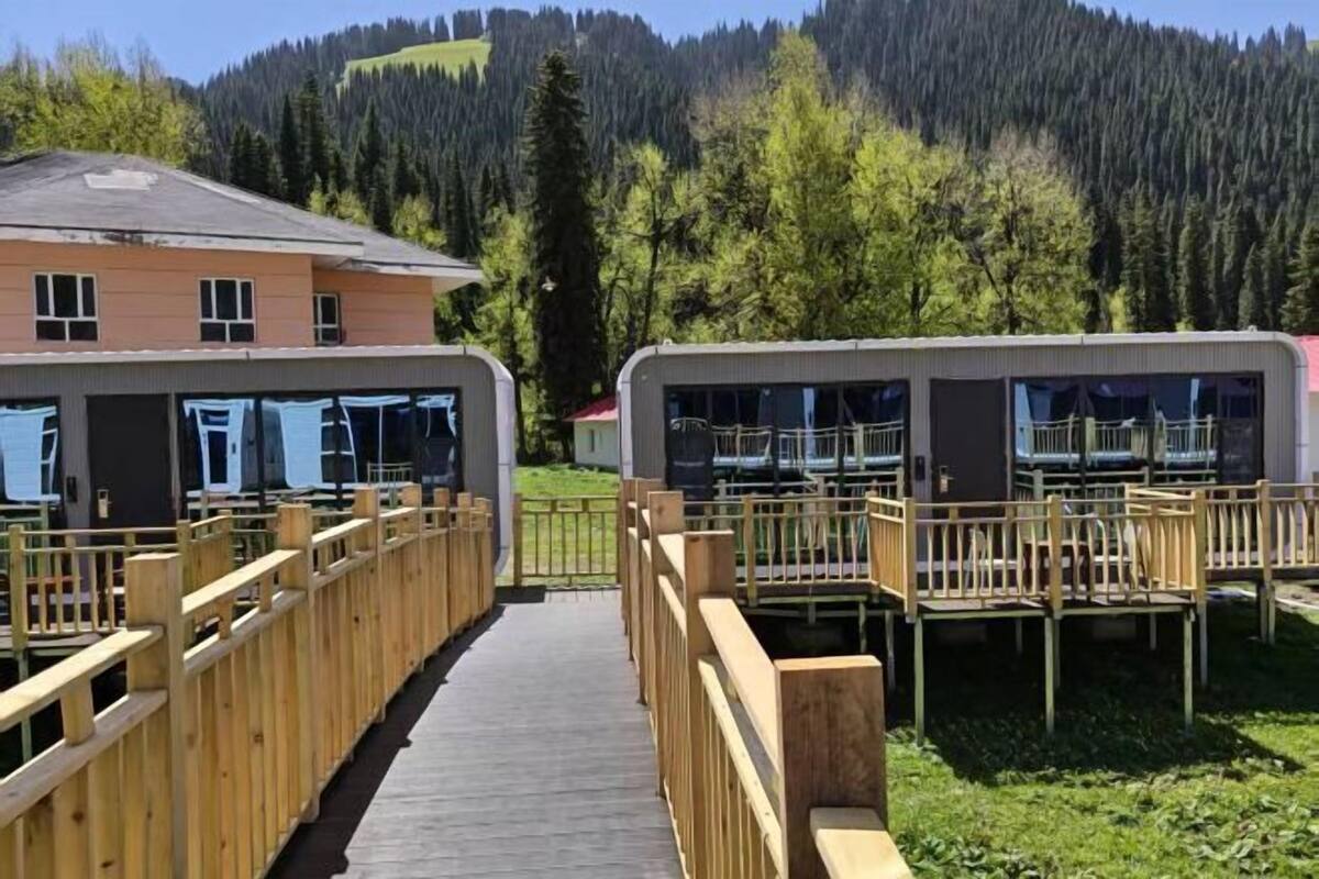 A row of cabins with wooden railings, a wooden walkway, and a mountain backdrop.