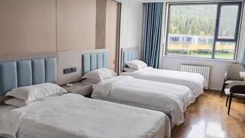 A hotel room with three beds, a window with a view of a forest, and a radiator.