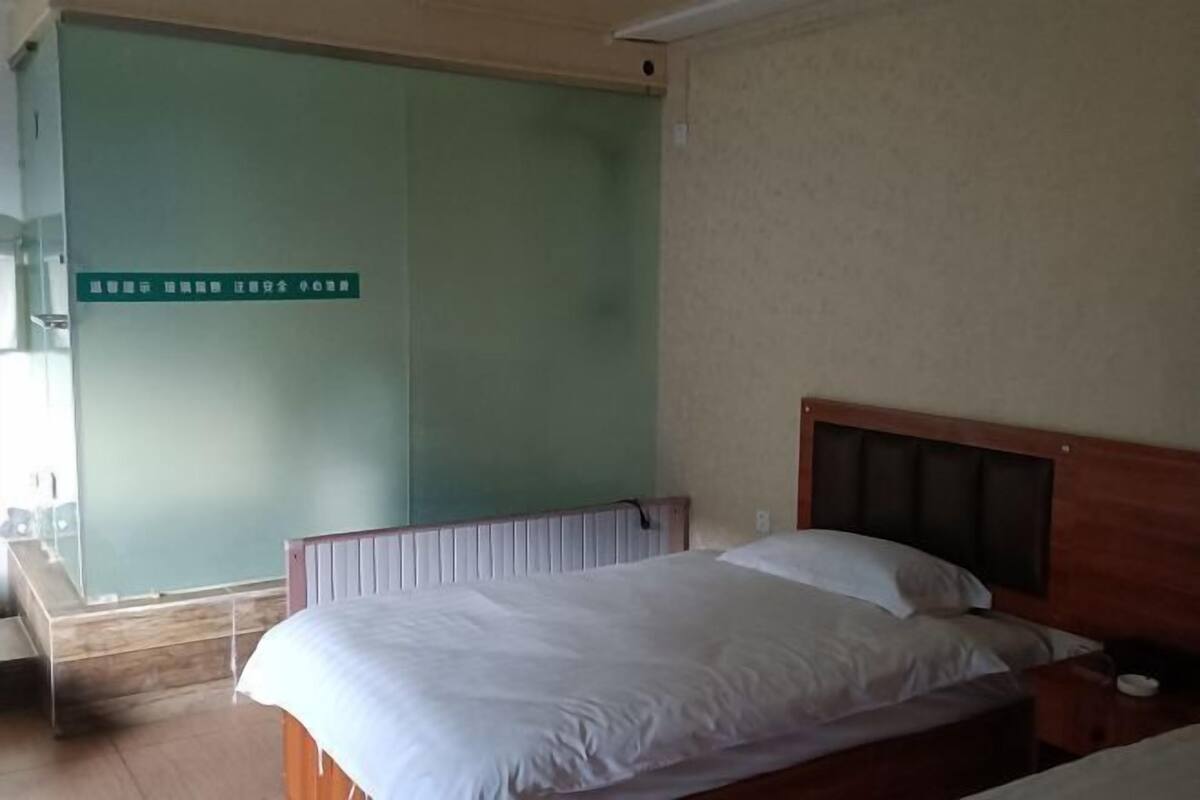 A bedroom with a wooden headboard, a bed with white bedding, a nightstand, and a green wall with a sign.
