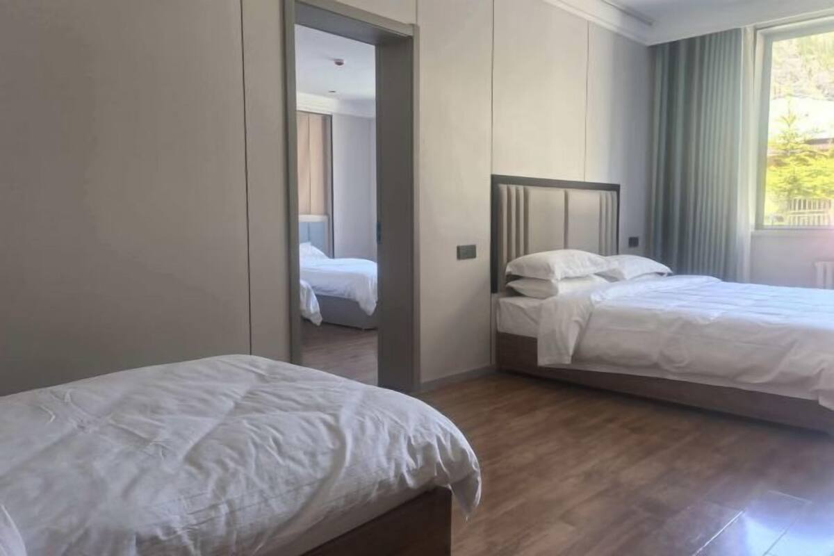 A hotel room with two beds, a wooden floor, and a view of greenery outside.