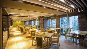 A modern dining area with wooden tables and chairs, large windows, and a stone wall. - Pulun Hotel (Shaoxing Didang Shimao Plaza) (Shaoxing)