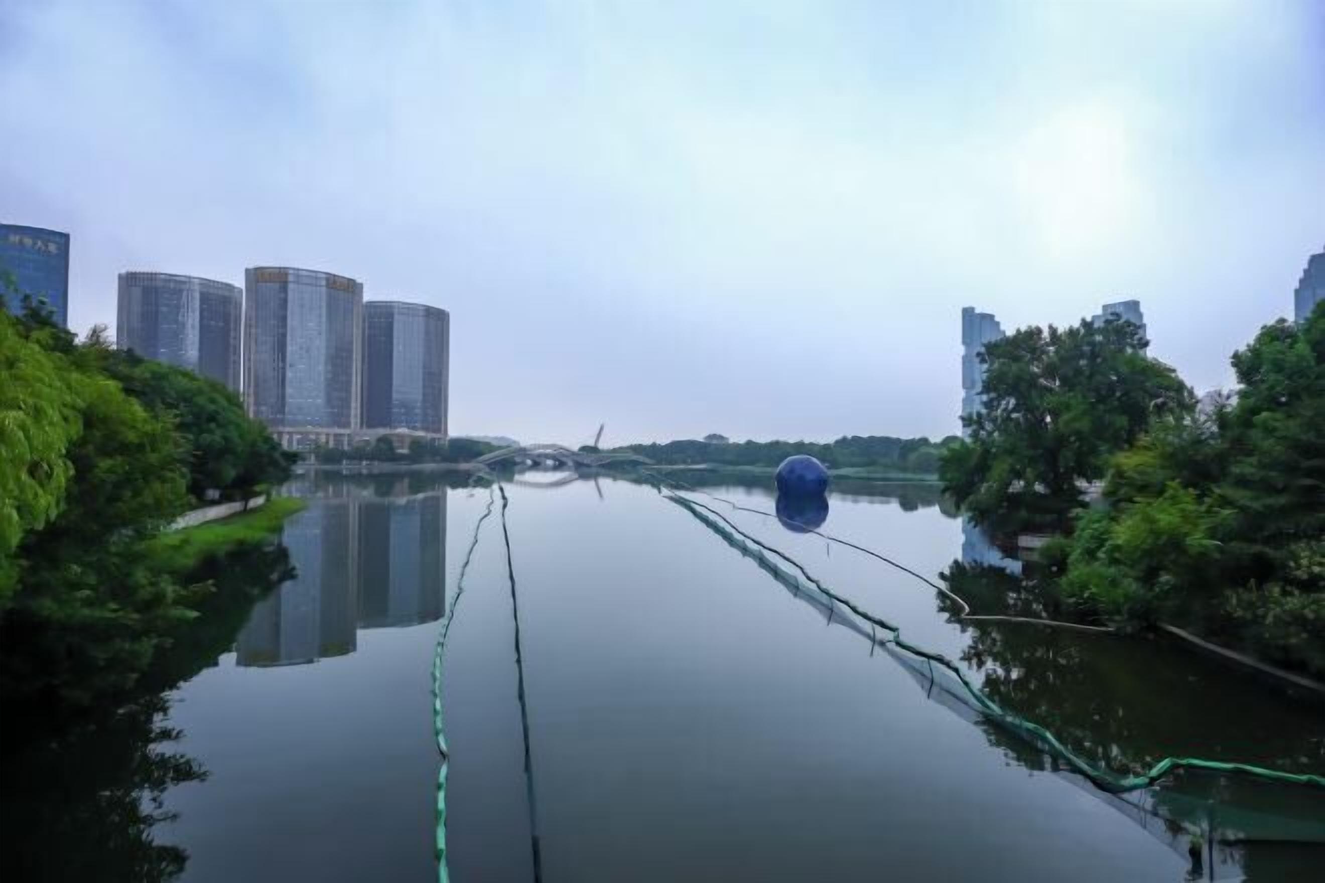 A calm river with buildings on the left and trees on the right.