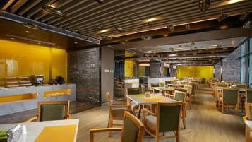 A modern restaurant with multiple dining tables and chairs, a counter with a coffee machine, and a stone wall.