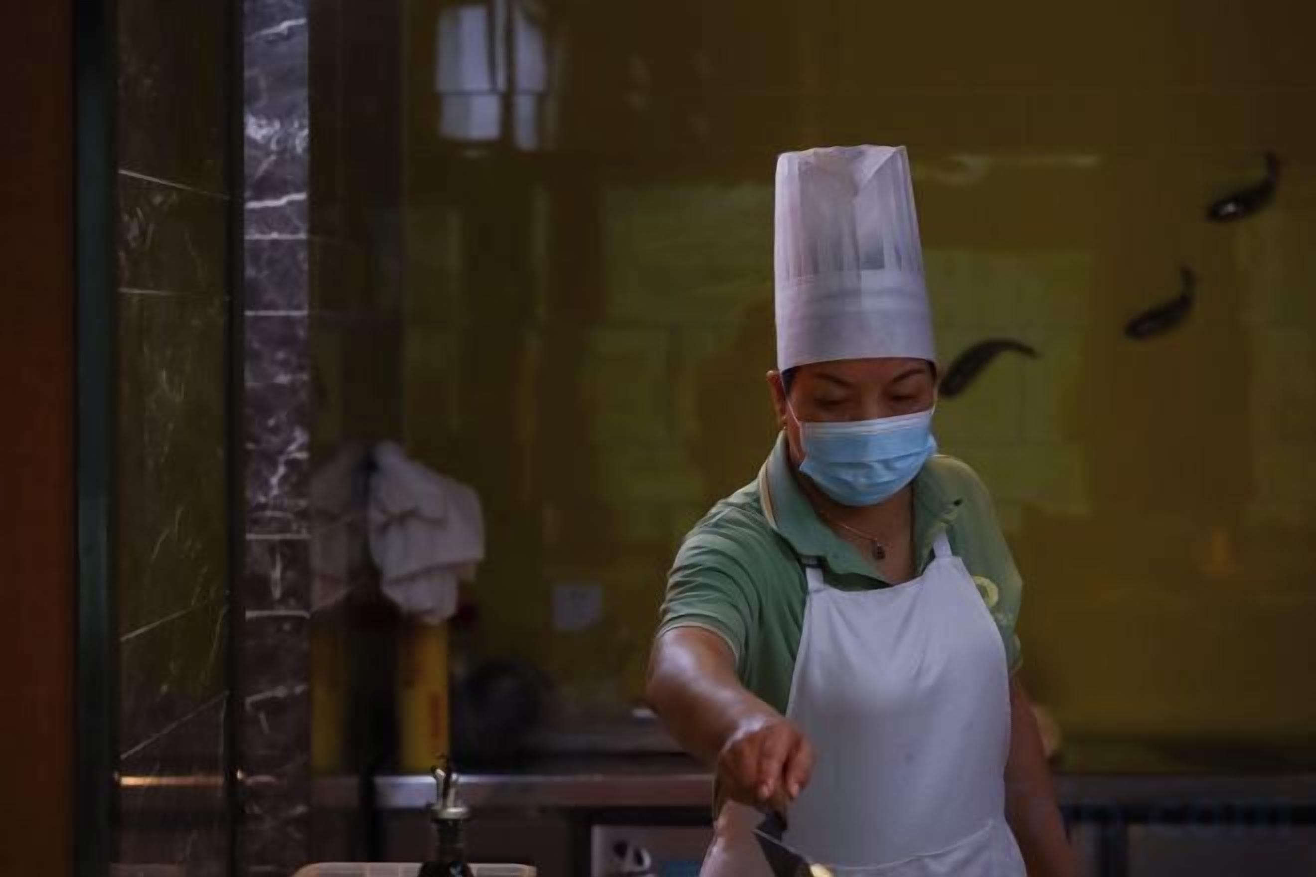 Um chef em ambiente de cozinha profissional, usando chapéu e avental de chef, com destaque para a área de preparo.