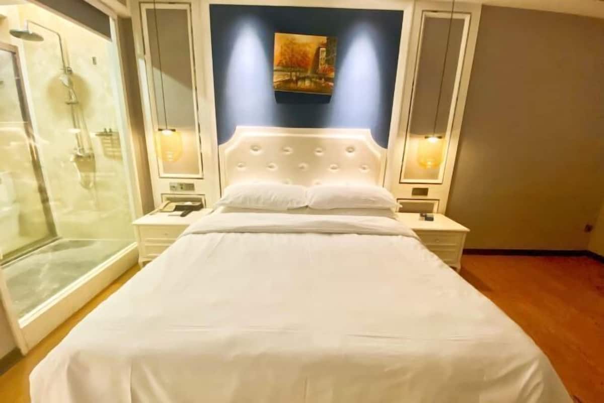 A hotel room with a large bed, a glass shower enclosure, and a painting on the wall.